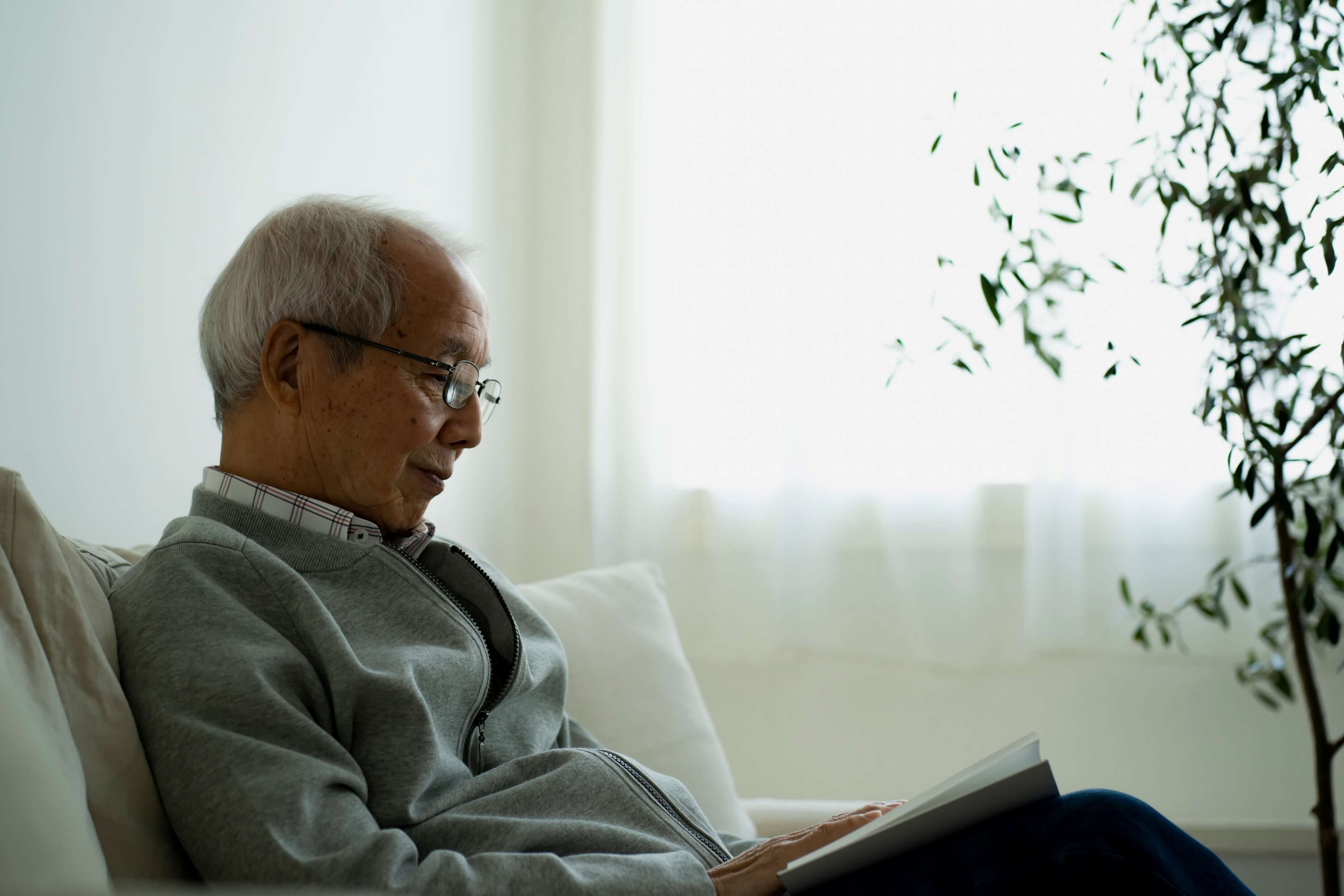 初老の男性がソファに座って本を読んでいる